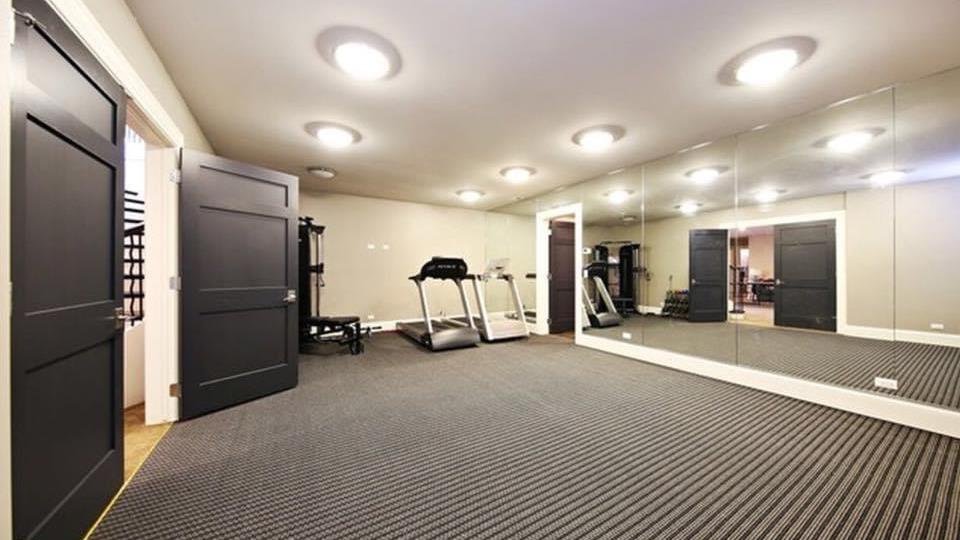 Custom home gym with mirrored wall, treadmill, and rubber flooring